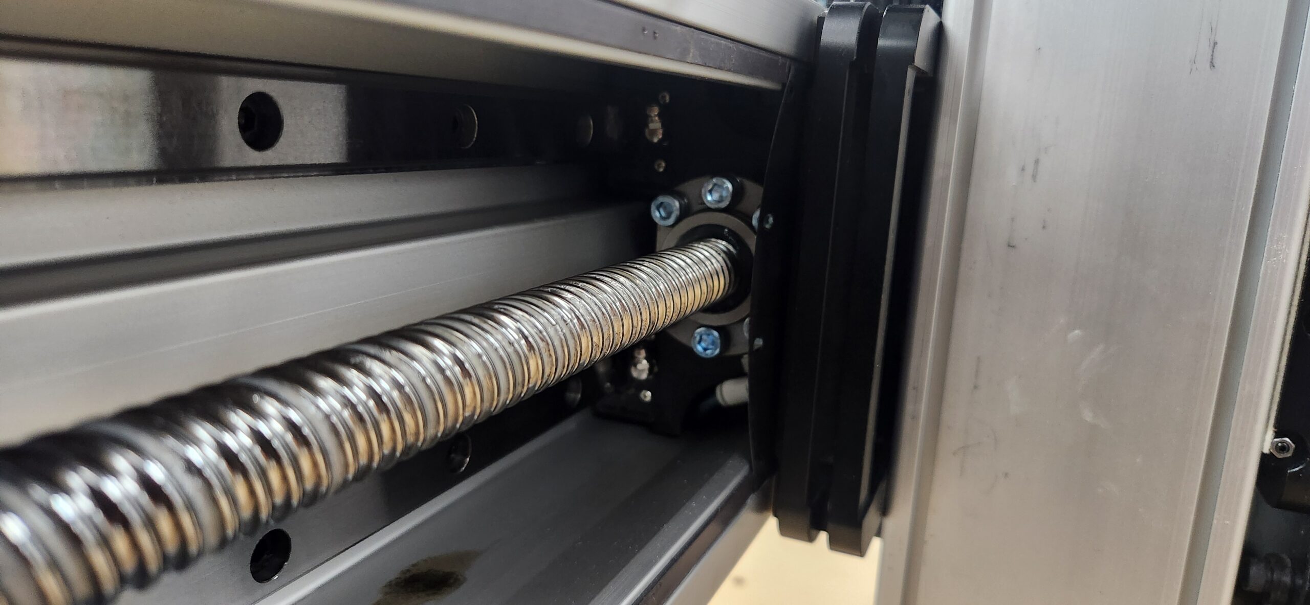 Close-up photo of a ball screw assembly on the Fusion Pro CNC machine, showing the linear rail, guide block, and dust management components.